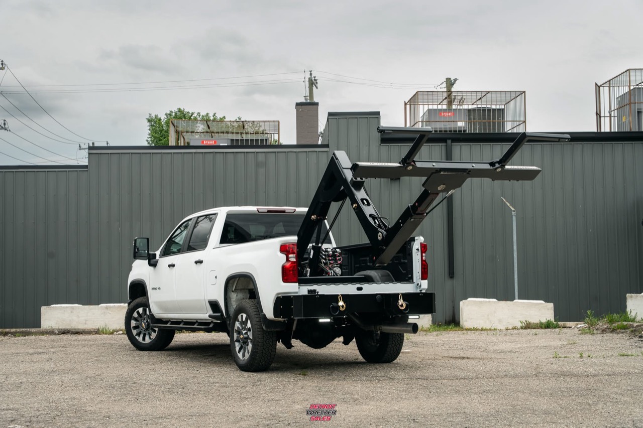Baby Gladiator fully raised above a white Chevrolet pickup.