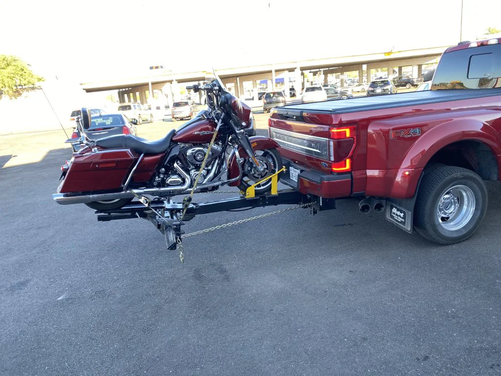 Red motorcycle secured on a Lil Hercules motorcycle attachment behind a red Ford pickup.